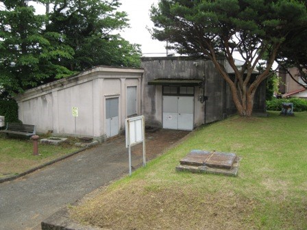 公園の片隅にある、木々や草に囲まれたコンクリート製の建物が二つ並んでいる様子を写した写真