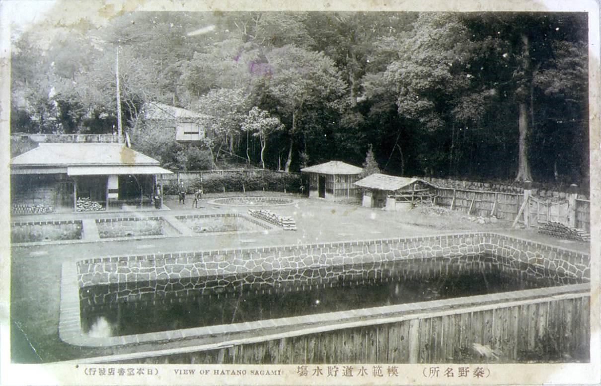 木々に囲まれている複数の建物と、石組みの池や柵に囲まれた広い庭を写した古いモノクロ写真