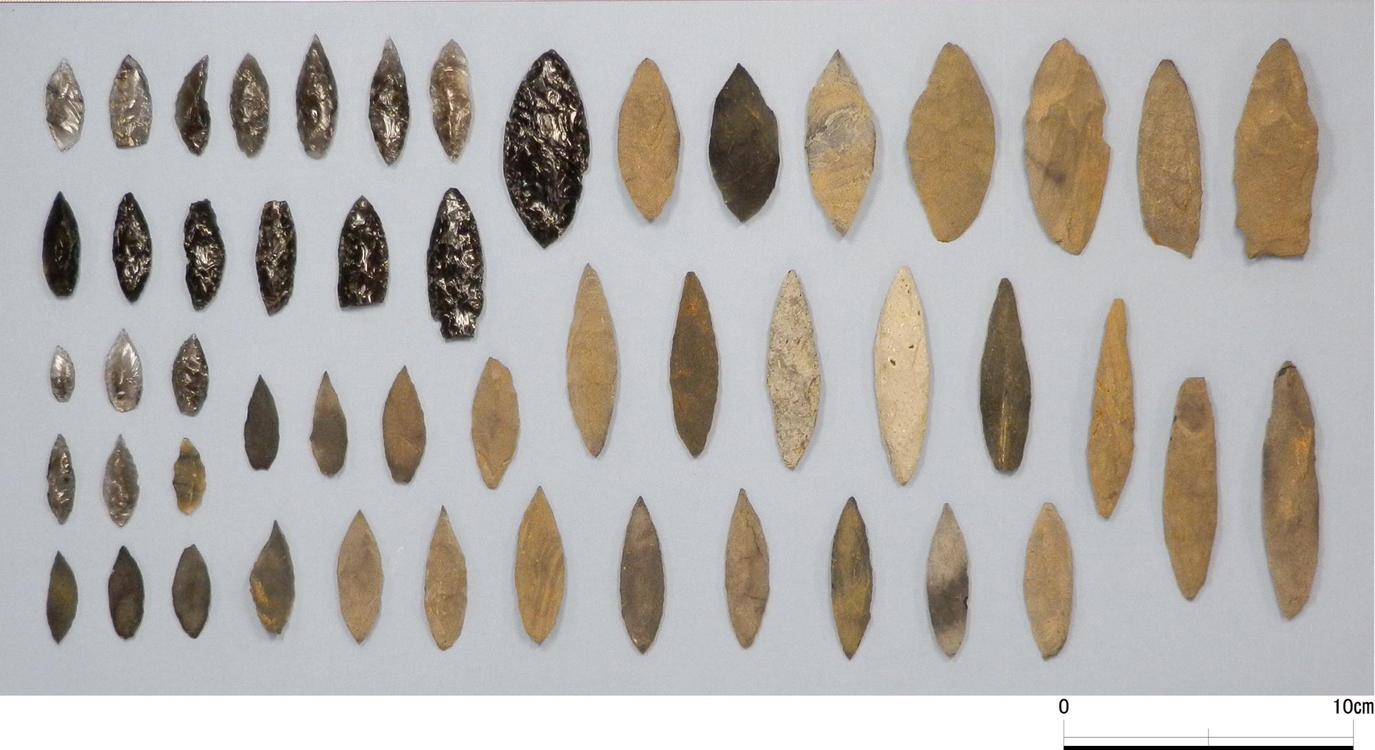 黒や茶色など、色も大きさも様々なたくさんの槍先形尖頭器が美しく並べられている写真