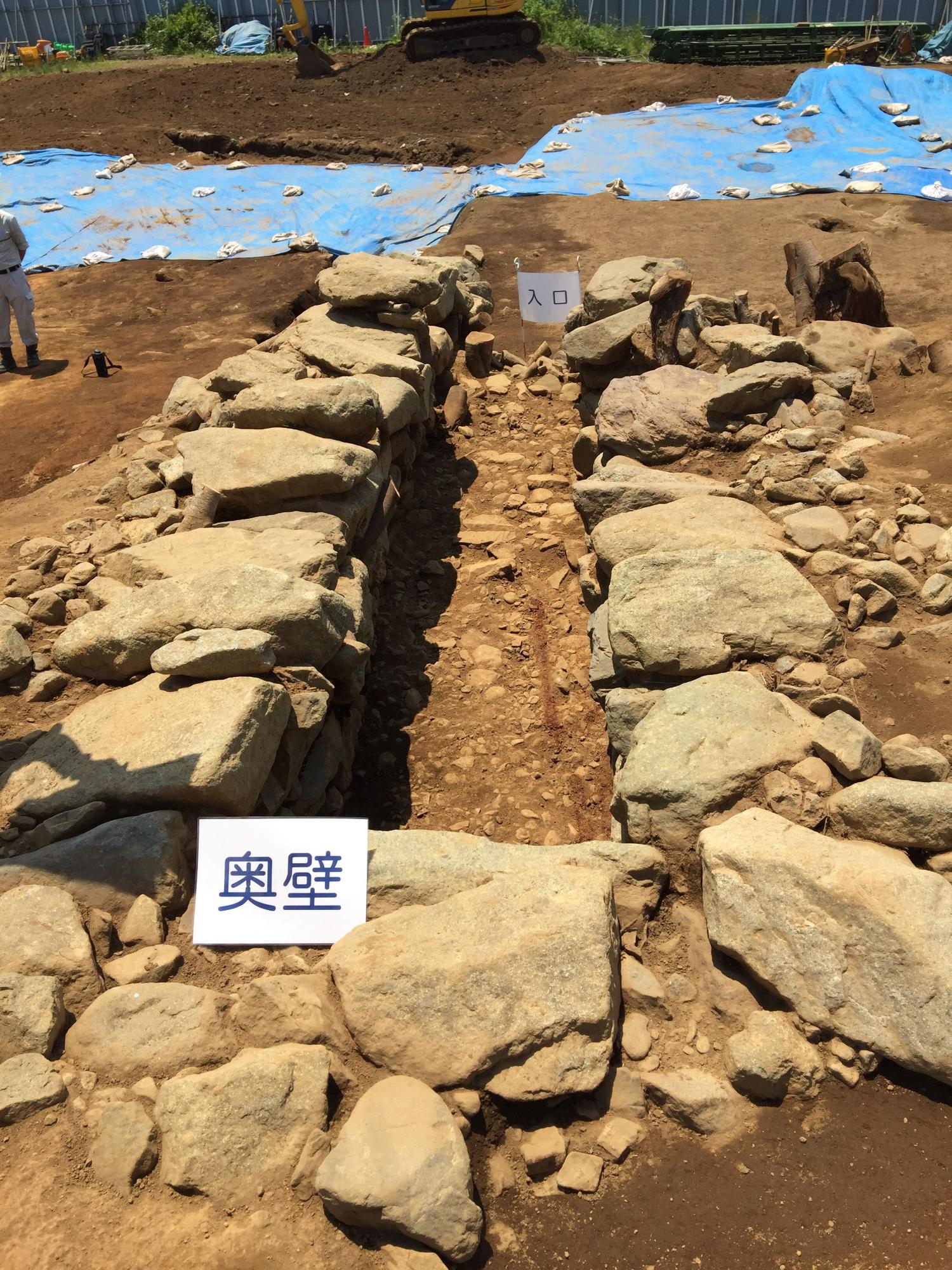 手前側に「奥壁」奥に「入口」と書かれた白い紙が立てられた、入口が開いた長方形に大きな石を並べた石室の写真