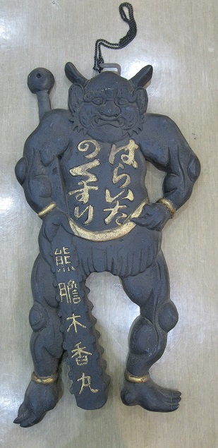 金棒を持った鬼の全身をかたどり、胸部分に「はらいたのくすり」と黄色の文字で書かれた、黒い掛け看板の写真