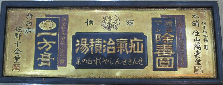 金色の背景に、黒い文字や、金色で文字が書かれた黒塗りの四角が描かれた、横長の掛け看板の写真