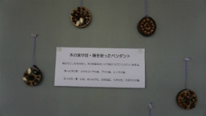 制作物の丸いペンダントが4つ、説明が記載された四角い紙を囲んで、ピンに吊り下げて展示されている様子の写真