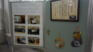 横並びに置かれた展示パネルに、授賞式の写真と説明書き、額に入った表彰状とクリスマスの飾りが展示されている様子の写真