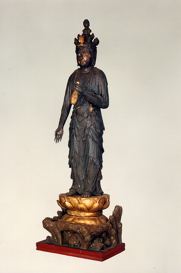 円形の光背を頭上にいただく、古びた木彫りの仏像を正面から撮影した写真で、左手には何かを持っていたような跡があり、台座の上に立っている木造十一面観音菩薩立像の写真