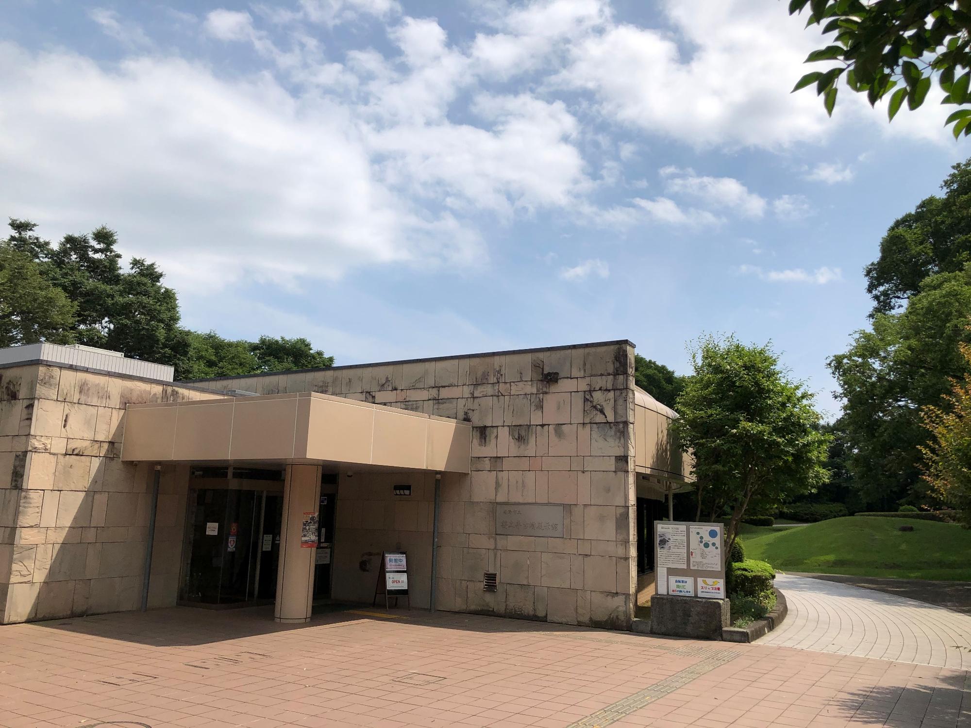 御影石風のタイルが貼られた建物と、その横にある緑豊かな公園の入り口の写真