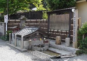 竹垣の前に文字が書かれた案内板が設置されており、その前に柵で守られた、石組みと水路があり低い屋根がついた小さな建造物がある写真の下に「弘法の清水（臼井戸）」と書かれた画像