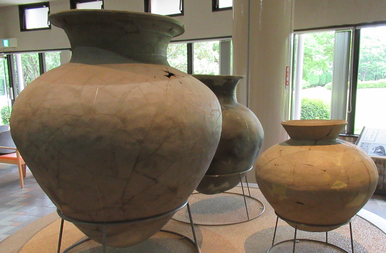 展示室の床に、それぞれ金属のフレームに立てられ大きさの異なる3つのつぼ型の土器が展示されている写真