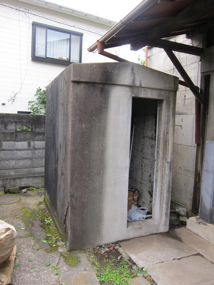 開いている扉の内部にはゴミらしきものが置かれている長方形のコンクリート製小屋を写した写真