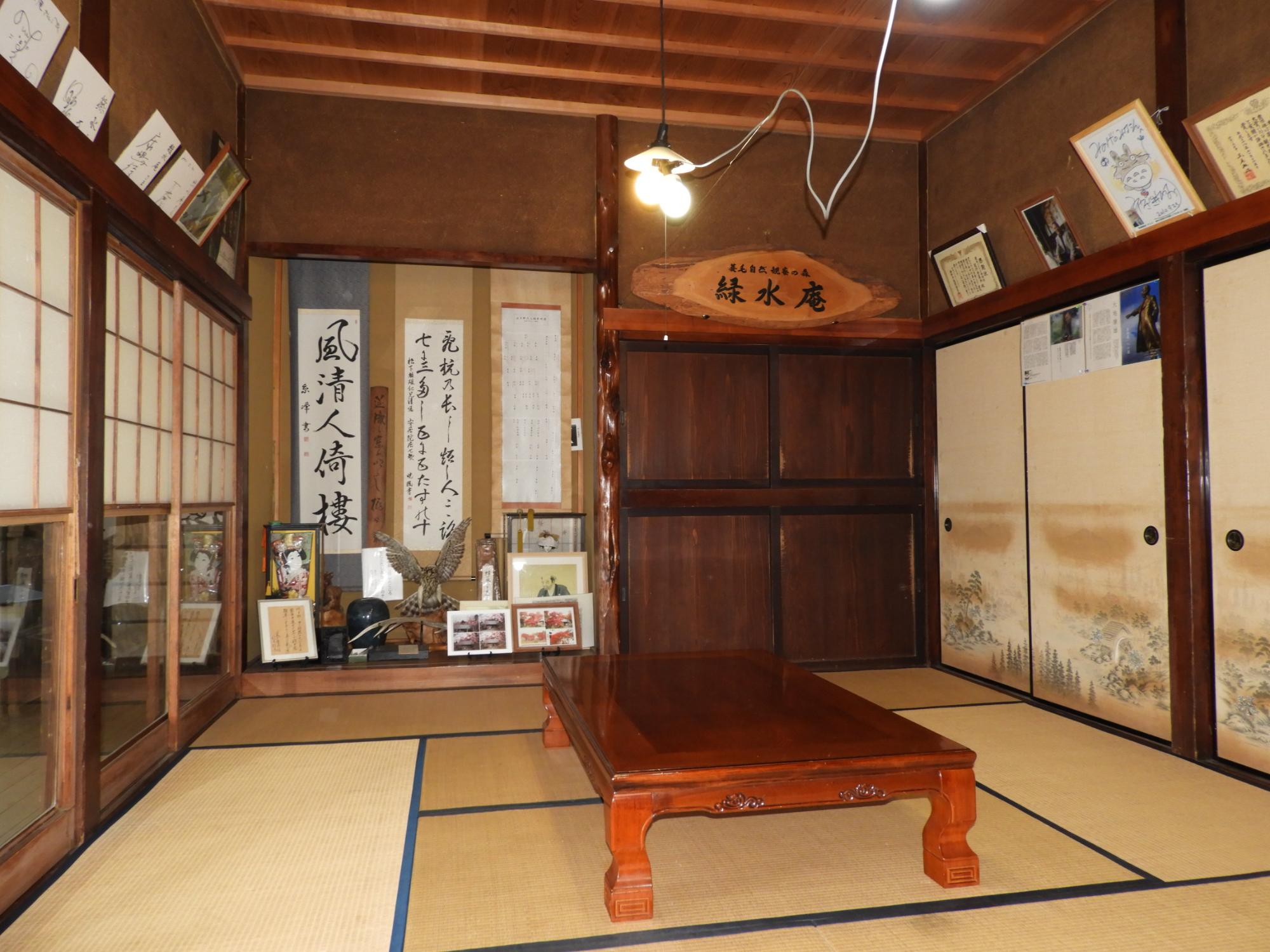 日本家屋の和室の室内を撮影した写真で、部屋の中央には脚が太く低い座卓が置かれ、壁は土壁、天井は木製の板張りで、正面奥と右側には襖や障子がある写真