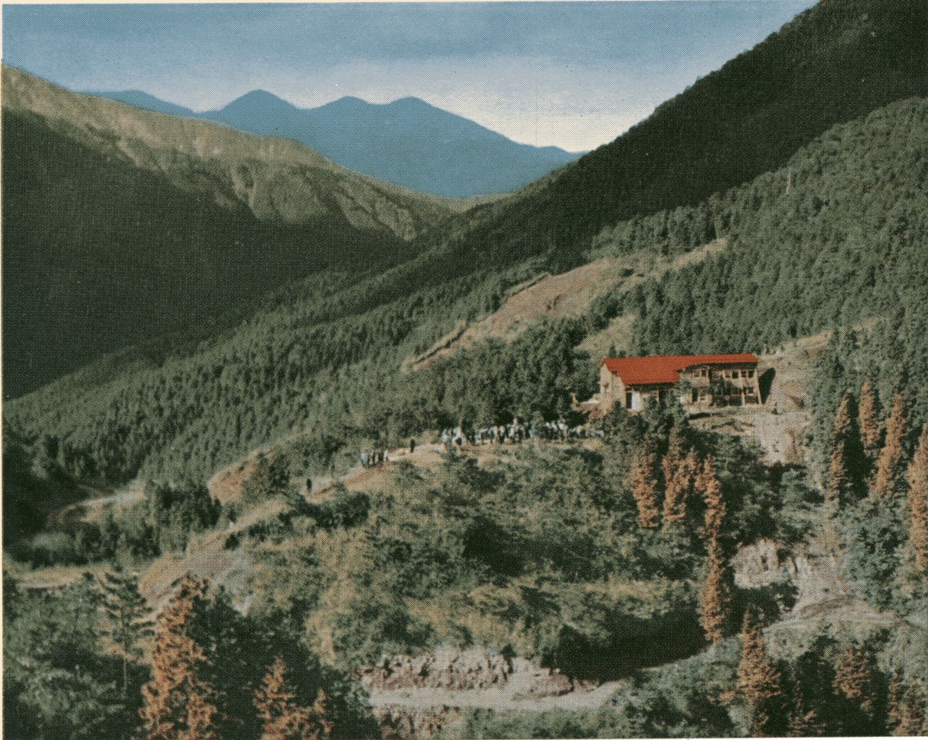 山間部の斜面に建つ赤い屋根のヤビツ山荘と、その手前の広場に集まる多くの人々を捉えた写真