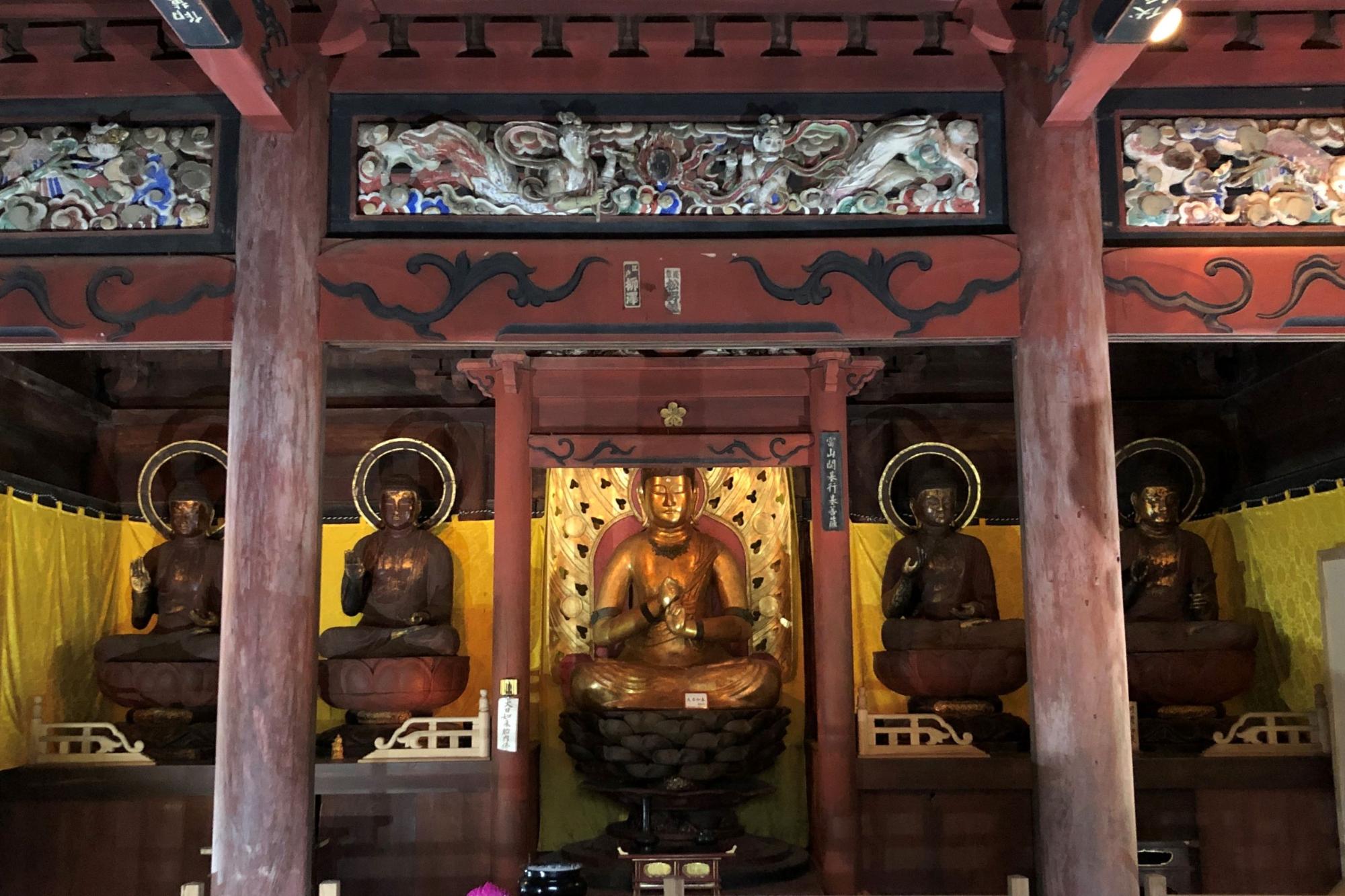 仏殿の内部で、光背にハート型の飾りが施された金色の仏像が蓮華座の上に結跏趺坐で安置されている様子を写した写真