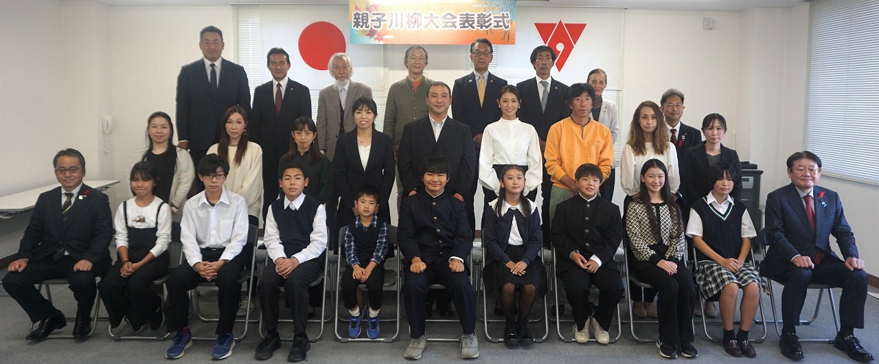親子川柳大会表彰式と書かれた横断幕の前で、前列の椅子に入賞者の子どもたちが座り、その後ろに保護者や後援団体の方々が立ち3列に並んで写した記念写真