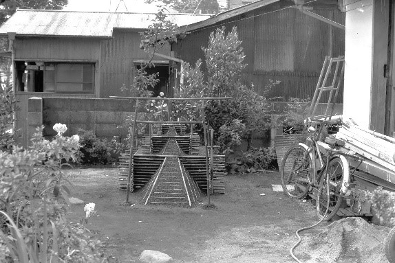 瓦屋根の家屋の前庭に組み立てられた竹製の盆の砂盛の白黒写真