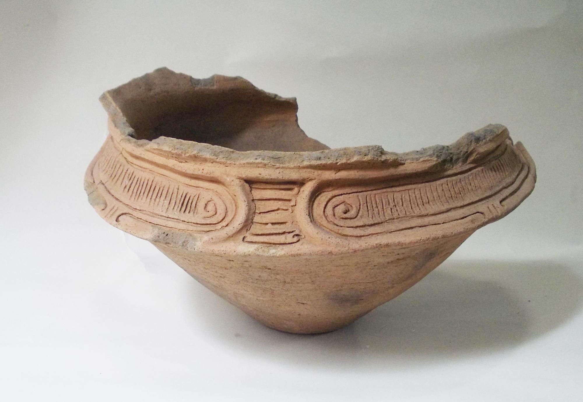 胴部に渦巻き模様や階段状の文様が繊細に刻まれており、口が大きく開き一部が欠けた土器の写真