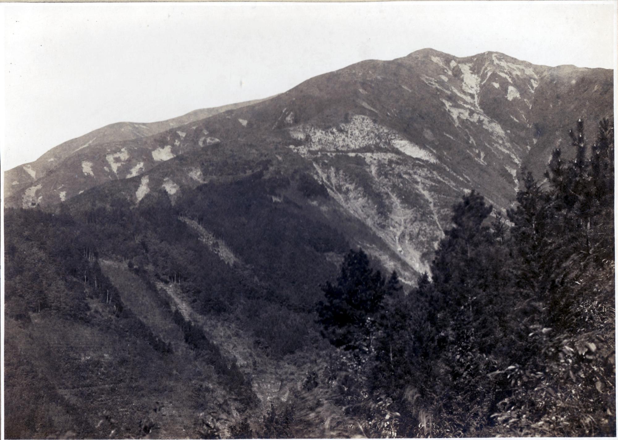 険しい山の山肌が露出しており、山腹には樹木がまばらに生えている様子が見える、丹沢山崩れの白黒写真