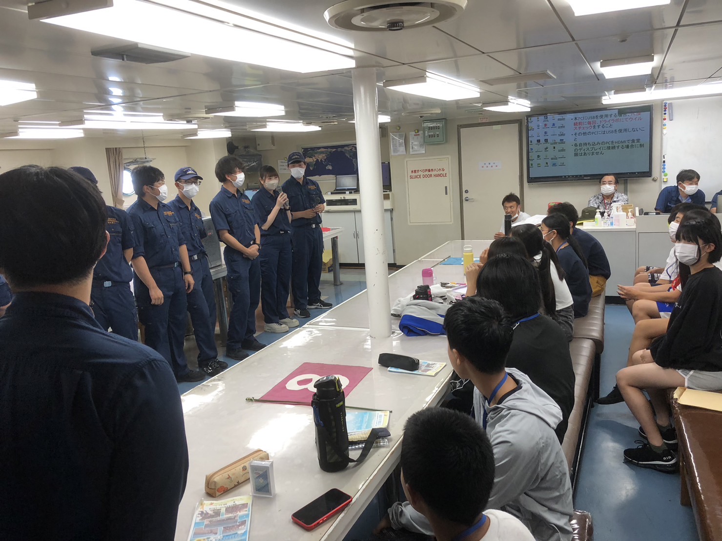 紺色の制服を着た望星丸の練習生たちが横一列に並んで立ち、席に着いた参加者の子どもたちにクイズを出している様子の写真