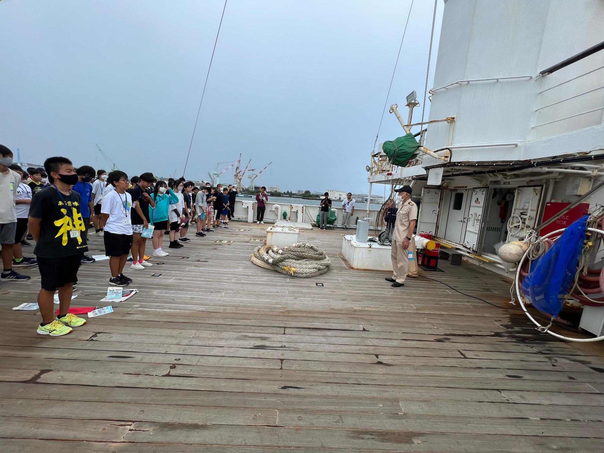 船のデッキに整列した子どもたちが、船長の男性と向かい合って立っている写真