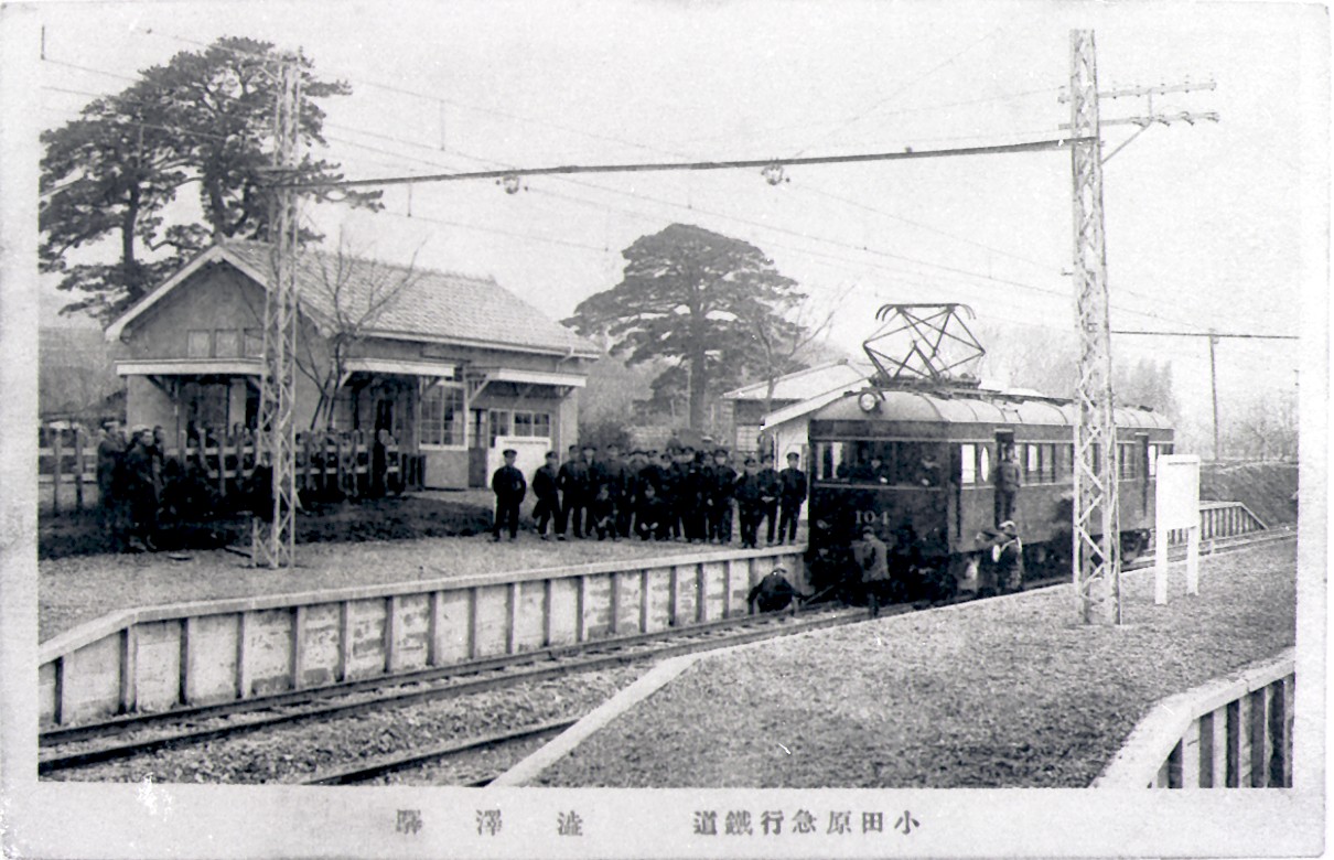 小田原電気鉄道の駅舎の前に電車が停車しており、線路の中やホームにたくさんの人が集まっている様子の写真