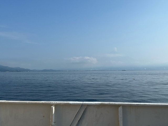 船のデッキから見た、穏やかな海と遠くに連なる山々が広がる風景の写真