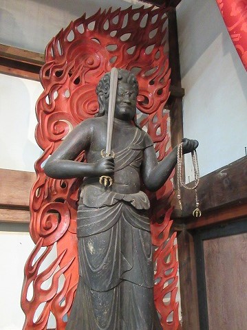 燃え盛る炎を背負い、右手に剣を掲げ、左手に羂索を握っている、険しい表情の仏像を捉えた写真