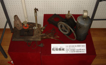 たばこの葉の乾燥に使われたと考えられる、複数のメーターやパイプがついた錆びた古い機械が展示されている写真