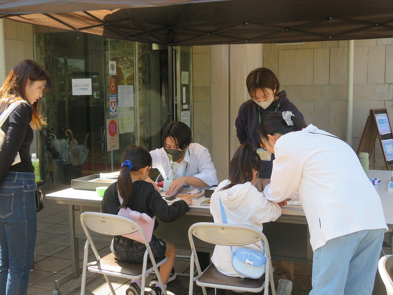 建物の入り口前に設置された受付で、2人の女の子が用紙に記入をしている様子の写真