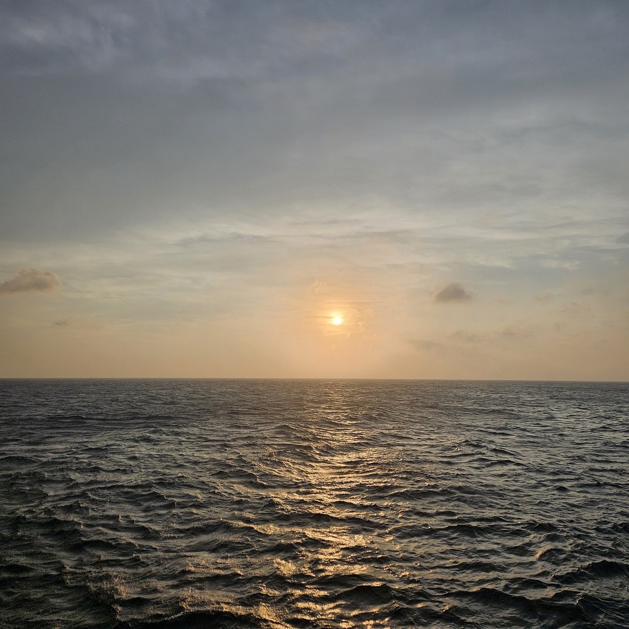 水平線の少し上に朝日が昇り、太陽の光が波の上に反射している様子が写っている写真