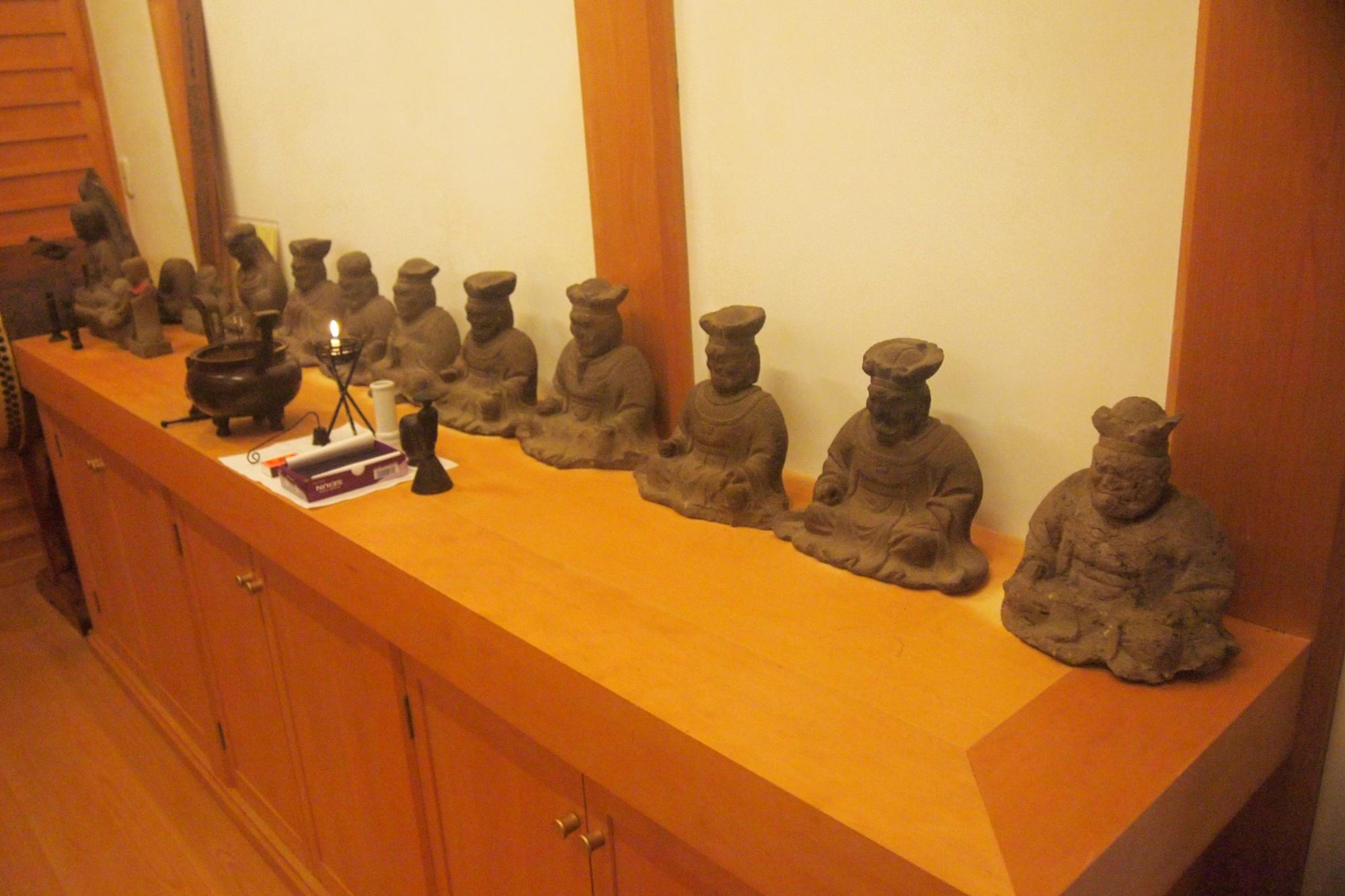 室内の木製棚の上に、それぞれが異なった表情とポーズで座禅を組むような小さな素焼きの仏像が多数並べられ、左端には香炉のような仏具が置かれている写真
