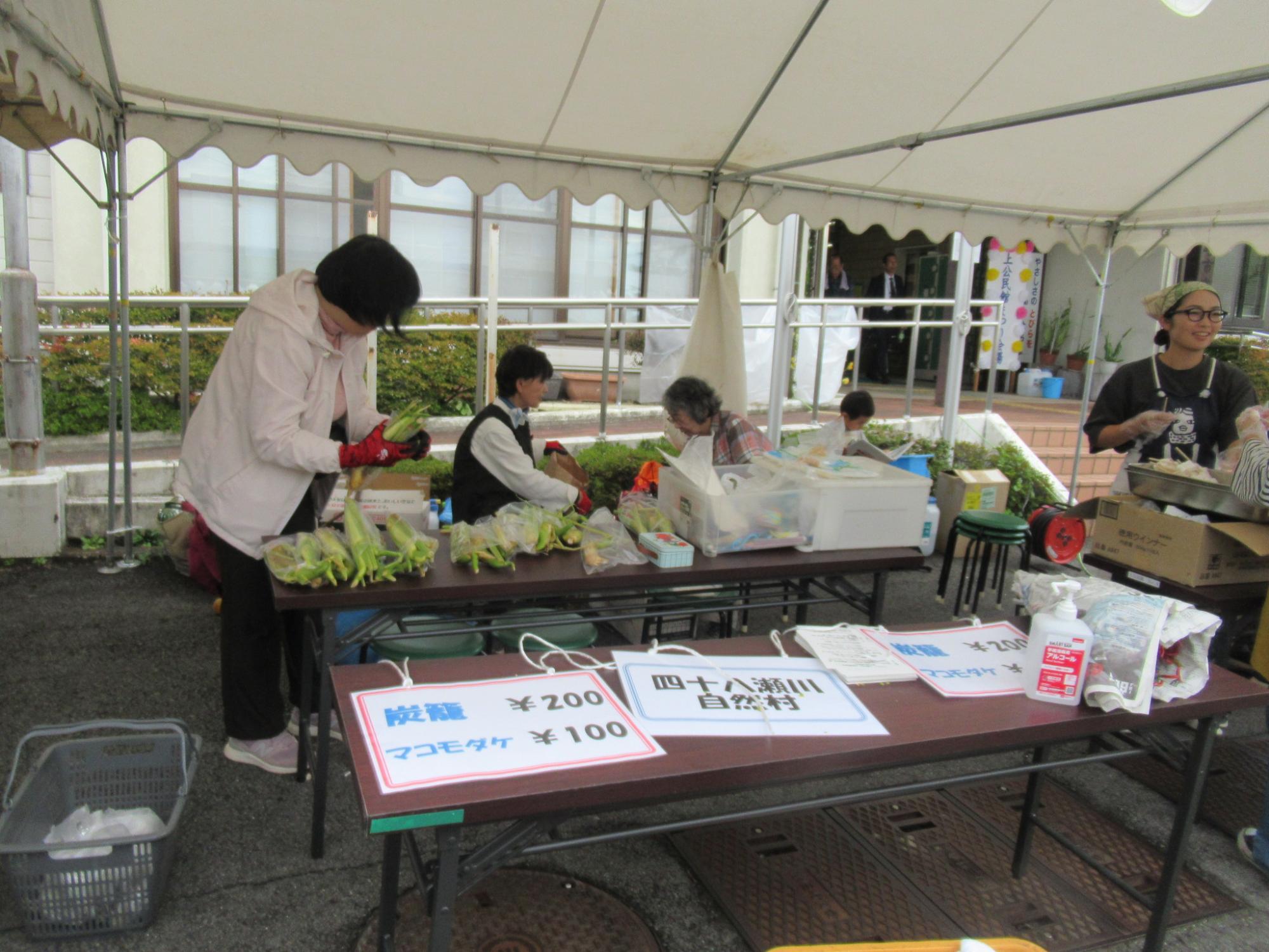 白いテントの下で数名の女性たちが、野菜の袋詰めなどの作業をしている様子の写真