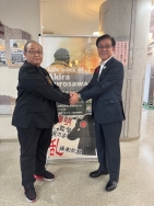 ポスターの前で、黒い服の男性と濃紺のスーツの男性が握手をしている写真