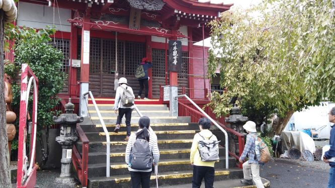 赤い柱と屋根が特徴的な寺院の建物に向かって、数人の参拝客が階段を上っている様子の写真