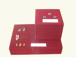 深紅の段状の台の上に様々な形のイヤリングや装飾品が並べられ、各段に白い説明書きが添えられている展示品のクローズアップ写真