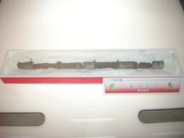 細長い銀装圭頭大刀が赤い箱に入れられ、その横には展示物の説明が書かれたパネルが配置されている博物館の展示写真