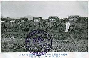 たくさんの人が立っている斜面の上に、4台の馬車が等間隔に並んでいる様子を写した白黒写真に「記念」と書かれた丸いスタンプが押されている画像