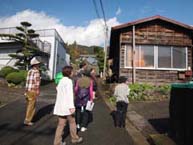 参加者たちがガイドに続いて、秦野葉のたばこ乾燥室の建物の外観を見学する様子の写真