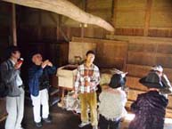 秦野葉のたばこ乾燥の内部で、数人の人々が曲がった梁や古い道具を興味深そうに観察する様子の写真