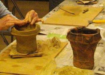 轆轤を使用せず粘土の形を作り上げる手法で、新聞紙が敷かれた作業台の上で女性が土器を製作している写真