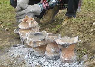 焼成した4つの土器が並べられており、後ろに厚手の手袋をはめた人がしゃがんでいる様子の写真