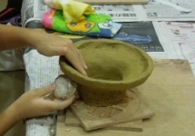 新聞紙を敷いたテーブルの木の板の上で鉢形の土器を作っている手元の写真