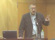 黒い上着を着た戸田哲也さんが、マイクの前に立ち、身振り手振りを交えながら聴衆に向かって熱心に講演をしている様子の写真