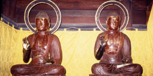 金色の布を背景に、後光を背に、蓮華座に座り、右手を上げた二体の木造仏像が安置されている写真