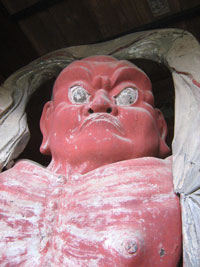 口を結び、憤怒の表情で正面を睨みつける、全身が赤く塗られた筋肉質な吽形（うんぎょう）像の胸から上の写真