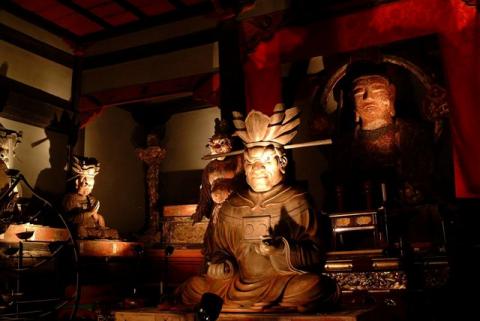 薄暗い室内に複数の仏像が並んで安置され、照明で照らされている写真