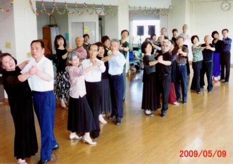 室内で、華やかな服装のたくさんの男女が、ペアになって社交ダンスの練習をしている写真