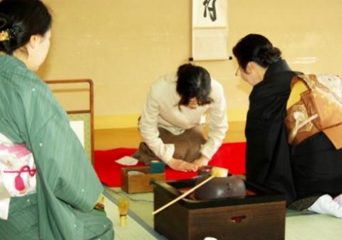 茶器などが準備された茶室で、2人の着物の女性と白いシャツの女性が畳に座り、茶道講座を行っている様子の写真