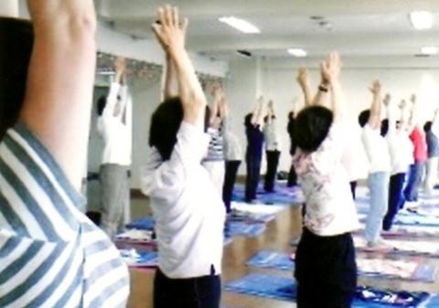 床に縦長のヨガマットを敷いて、たくさんの女性が並んで立ち、両手を天井に向けてポーズをしている写真