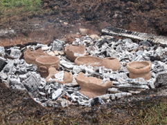 焼かれて白くなった木炭と灰の中に、複数の土器が置かれている、土器作りの焼成工程を捉えた写真