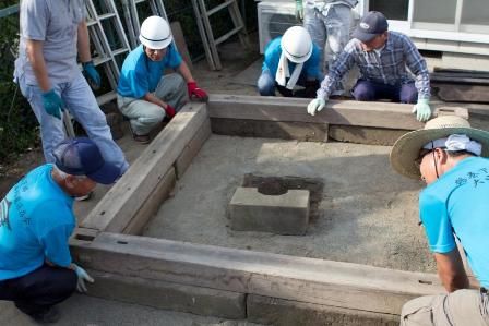 複数の作業者が、灯籠を囲む覆屋の基礎を組み立てている写真