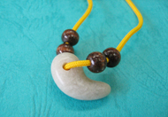 淡い緑色をした勾玉と、木目調の茶色い玉が黄色い紐に通された、手作りのネックレスを、青緑色の布の上で撮影した写真